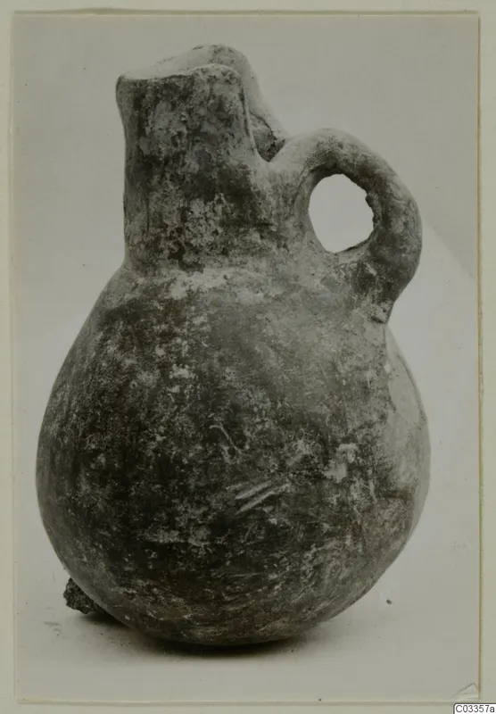 Pottery Red Polished III jug with a rounded body, narrow neck and loop handle, photographed on a pale background