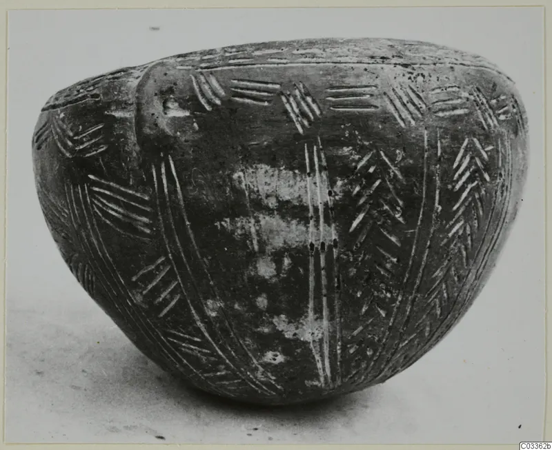 Dark polished bowl with incised herringbone and vertical line decoration, standing on a light surface.