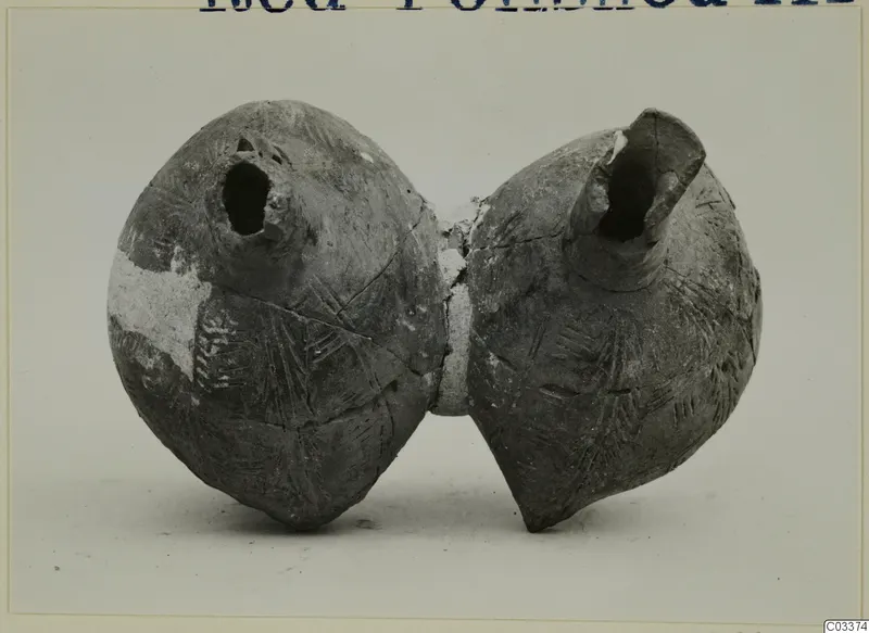 Pottery vessel of two rounded bodies joined at the middle, each with an open spout, standing on a plain background.