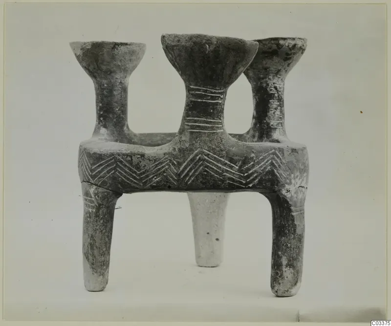 Grey pottery vessel with three flared mouths on a rectangular body and legs, with incised chevron decoration