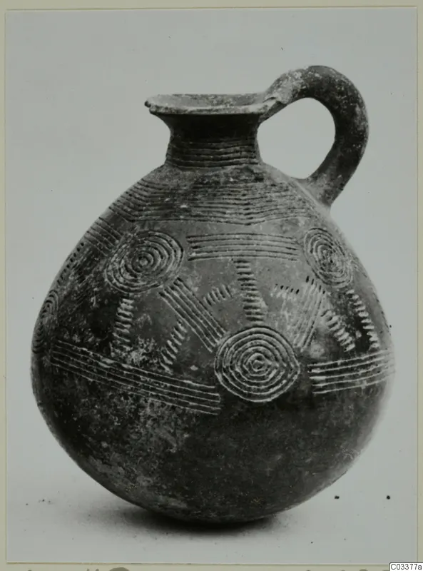 Pottery Red Polished II jug with a strap handle, incised with concentric circles and horizontal bands