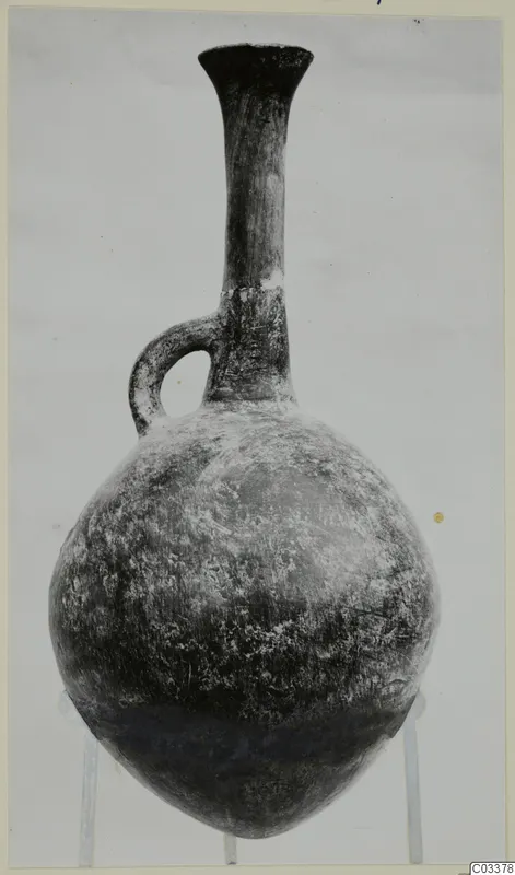 Pottery Red Polished II jug with a tall neck, flared rim and single loop handle, shown on a stand