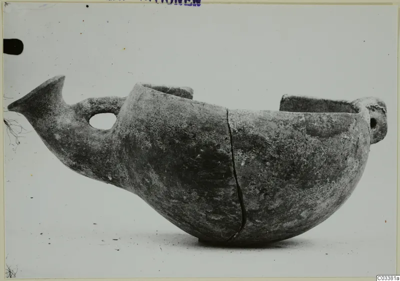 Pottery vessel in side view with a beak-like projection, a looped handle and two raised lugs at the top