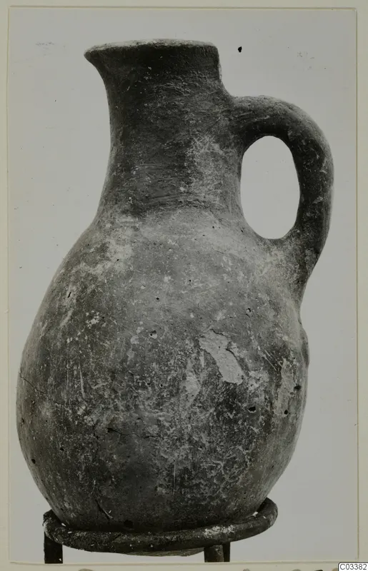 Red Polished III jug from Lapithos, with a single loop handle, standing on a metal ring stand