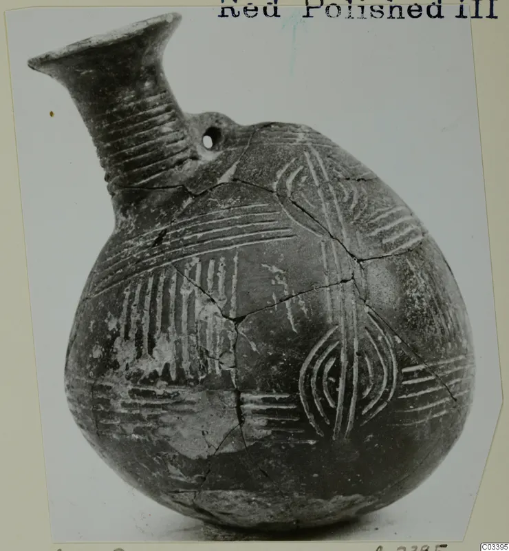 Red Polished III jug with incised bands, arcs and a small pierced hole, photographed on a card mount