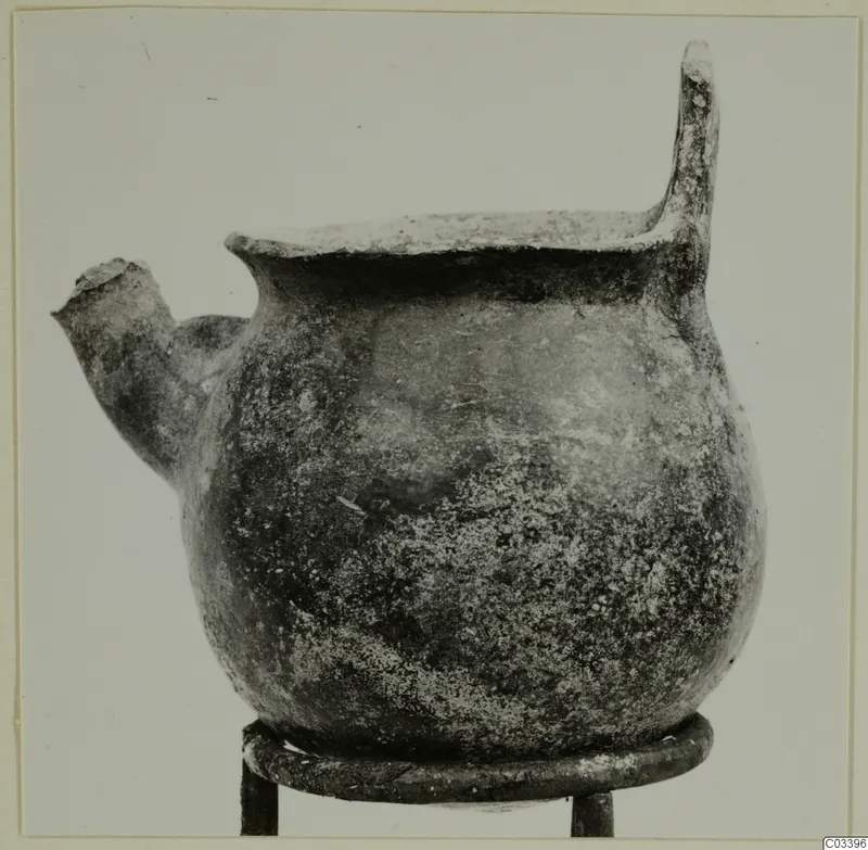 Pottery Red Polished II Bowl from Lapithos, shown on a metal ring stand, with a short spout and a tall handle