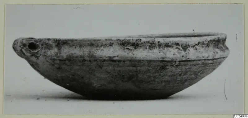 Plain white wheel-made pottery bowl with a small pierced handle, seen from the side.