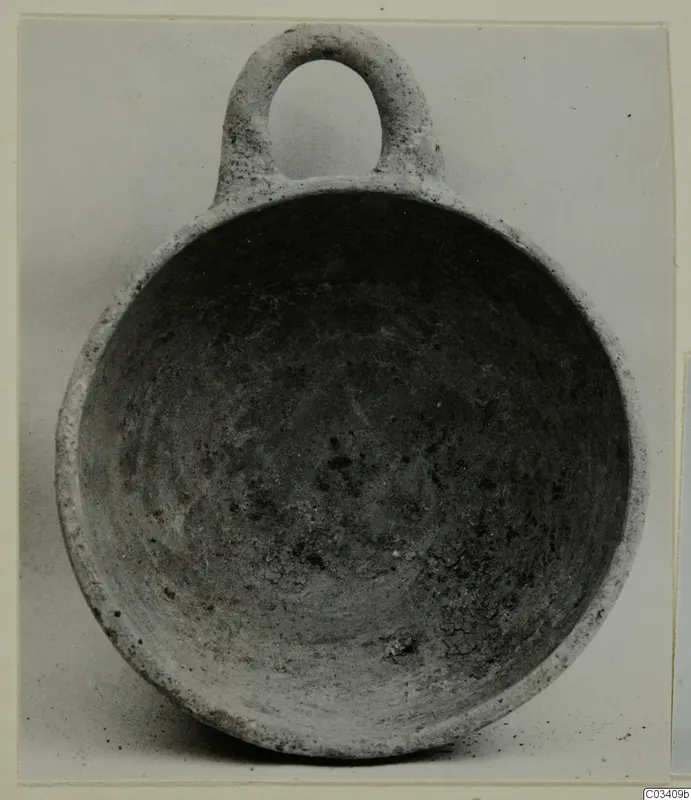 Pottery bowl with a single loop handle, plain white wheel-made, photographed from above showing its interior