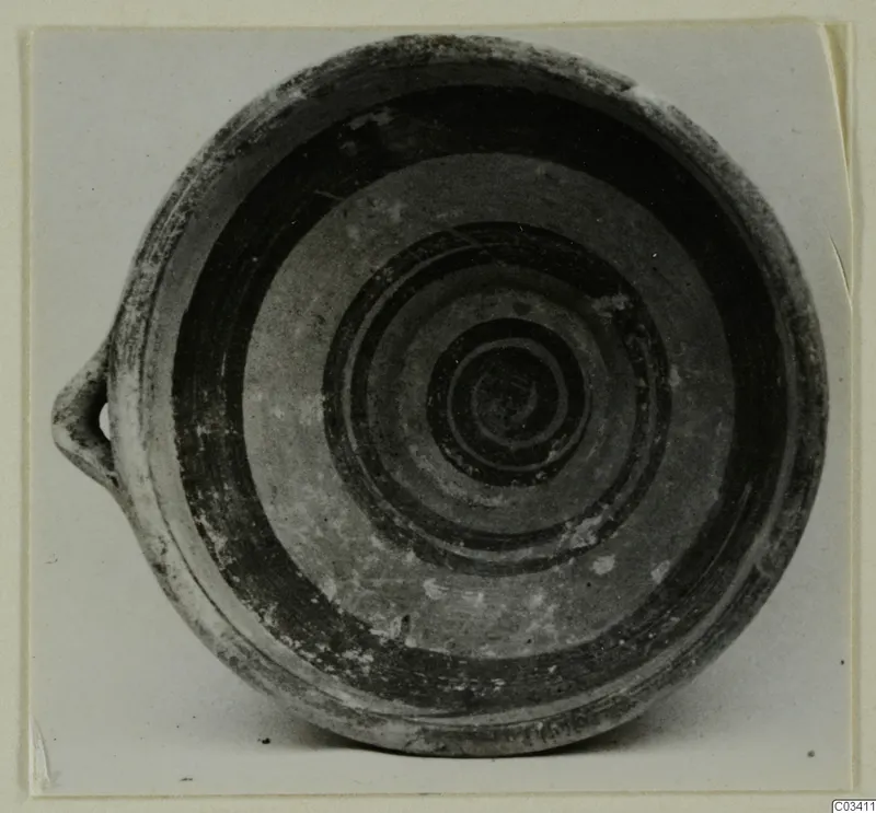 Bowl-jar with a single loop handle, its interior decorated with dark concentric and spiral bands.