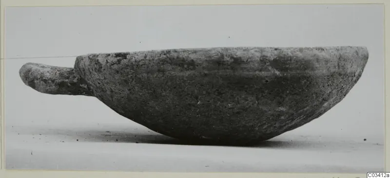 Hand-made pottery bowl with a short horizontal handle, shown in side view against a pale background.