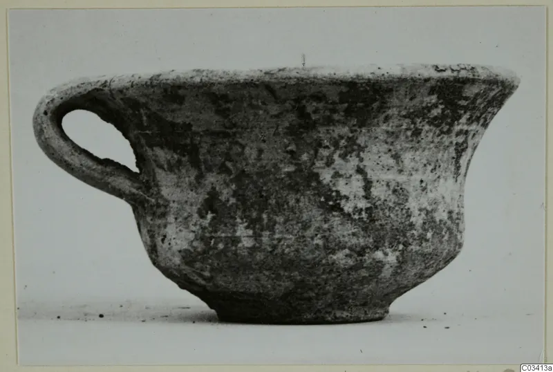 Plain white wheel-made pottery bowl with a single loop handle, seen from the side
