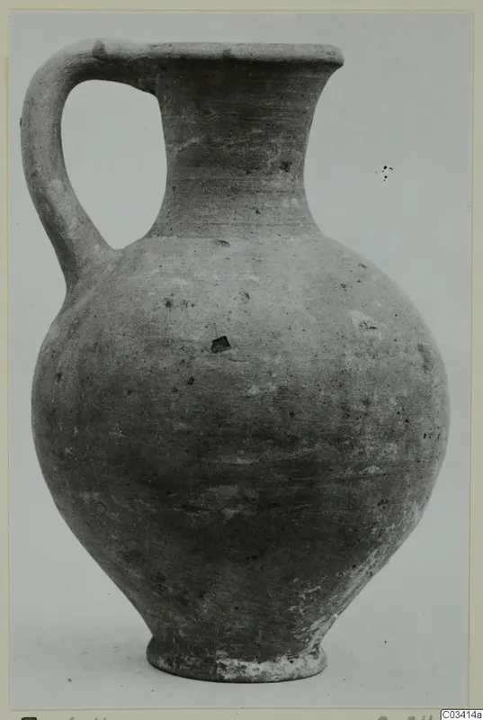 Pottery Plain White Wheel-made jug from Enkomi, with a single loop handle and tall neck, shown against a grey backdrop