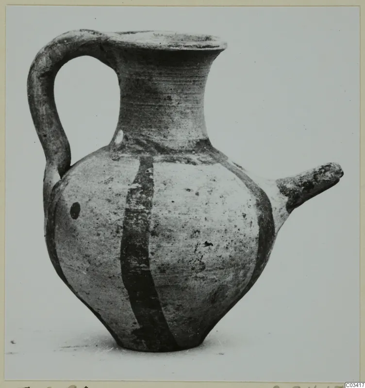 Wheel-made pottery juglet with a high loop handle, a side spout and two dark painted bands on a pale body.