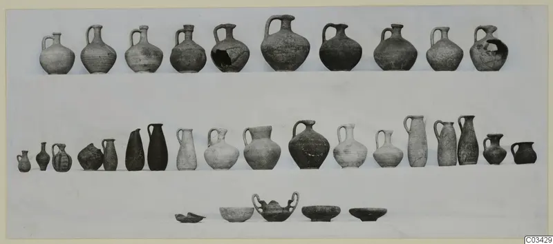 Rows of pottery jugs, bottles and bowls from Kountoura Trachonia, Tomb 2, arranged on a pale cloth