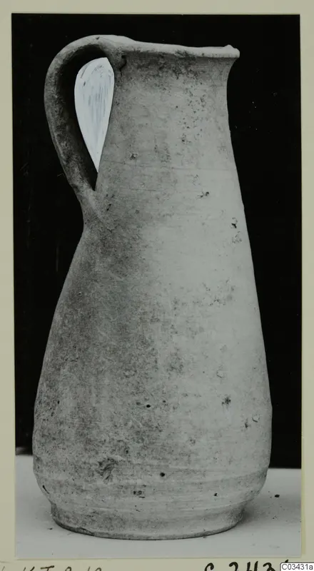 Pale single-handled jug with a tall neck and flaring rim, shown as a find