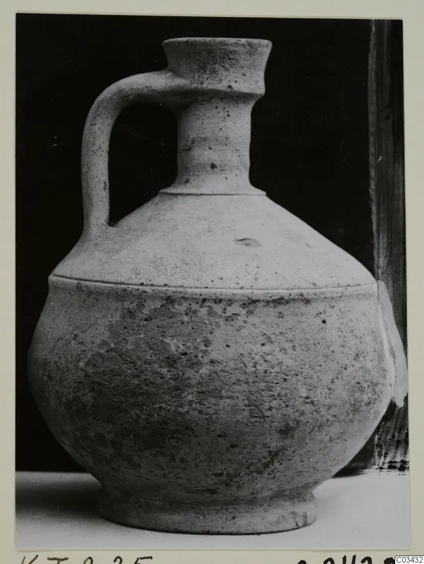 Single-handled jug with a narrow neck and flared rim, photographed against a black background.