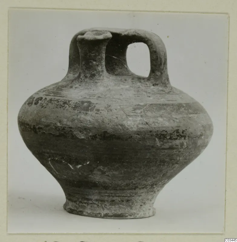 Pottery jug with a tall spout, a loop handle and a rounded body, photographed against a plain grey background.