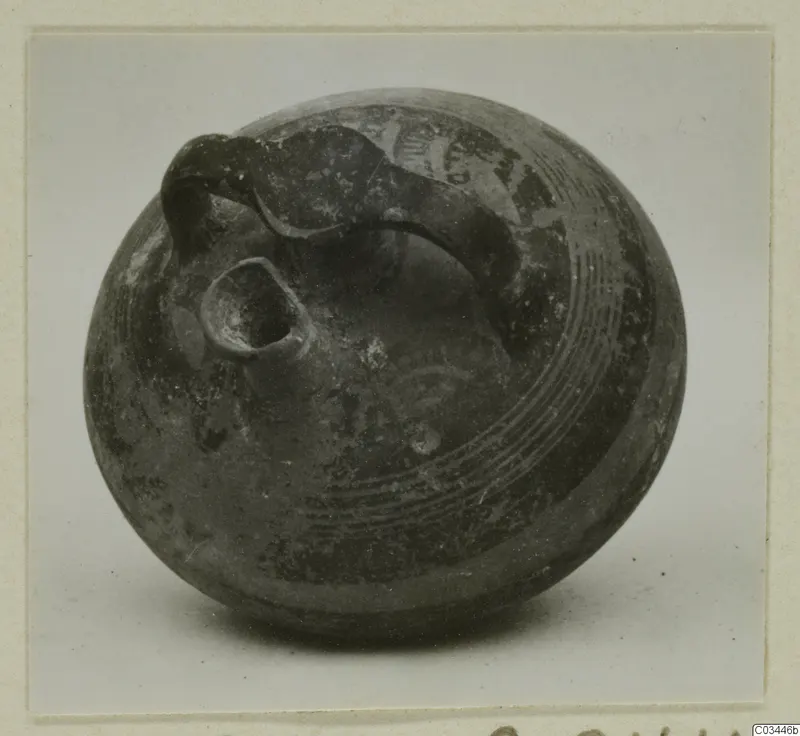 Dark grey pottery bowl-jar with a loop handle and small spout, with incised lines around the body