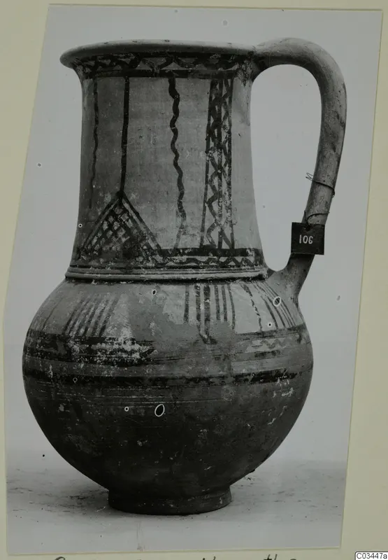 White Painted wheel-made jug with a strap handle, dark banded and hatched decoration on the neck and body