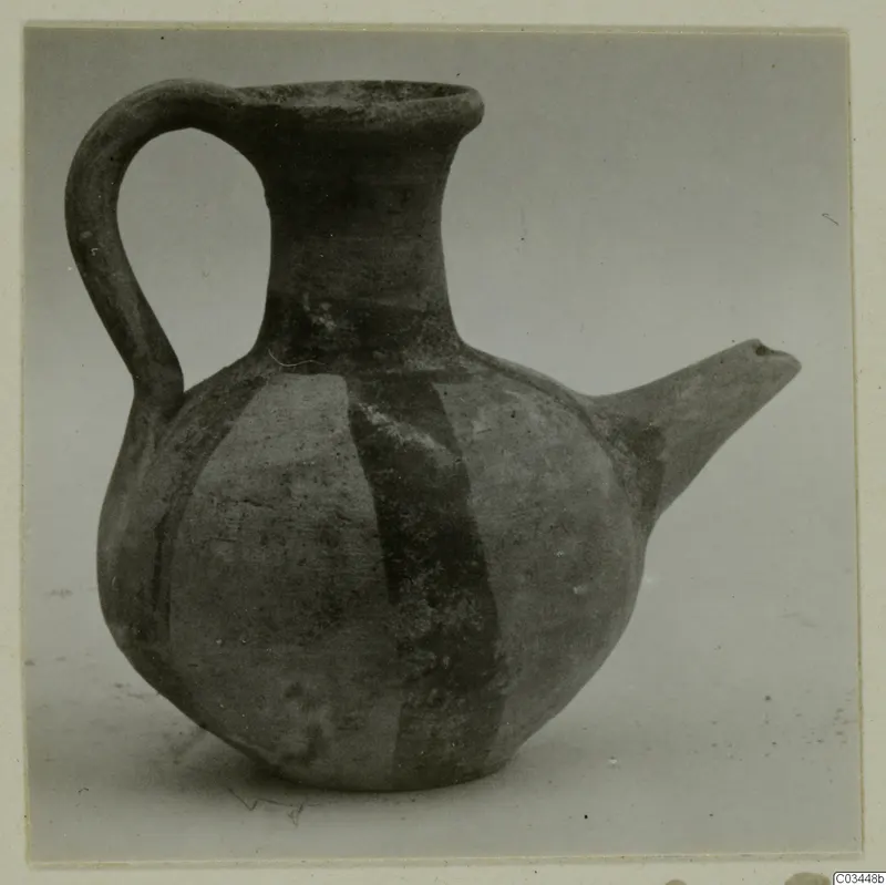 Round-bodied jug with a strap handle, a spout and a wide mouth, decorated with broad painted bands, photographed against a grey backdrop.