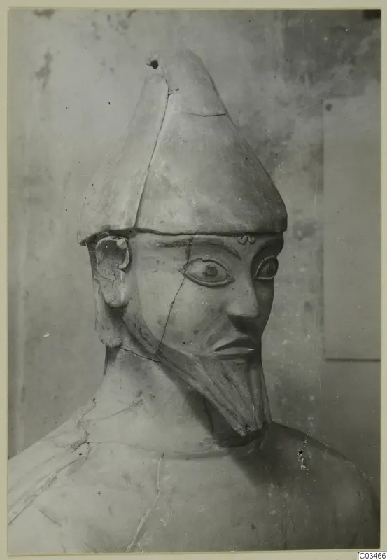 Terracotta statue from Ayia Irini with a tall conical headdress, large eyes and a long beard, seen from the chest up