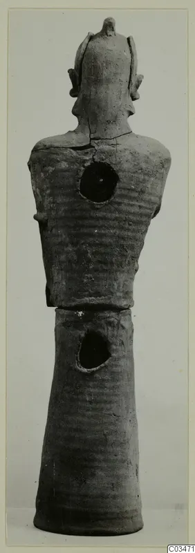 Terracotta figure with a ribbed upper body, arms at the sides, a crest-like top to the head and a tall tapering base.