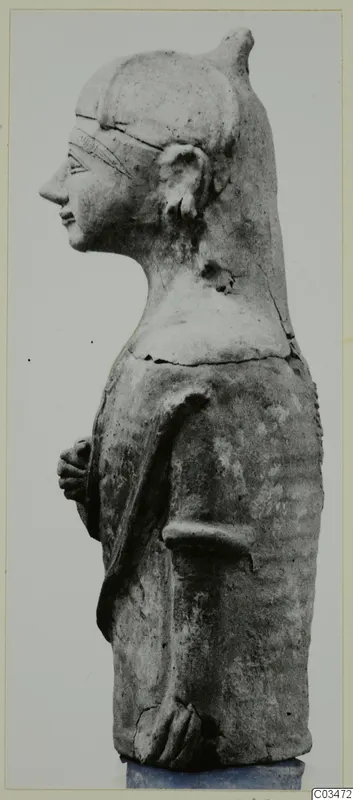 Terracotta Neo-Cypriote figure seen in profile, facing left, with a tall headdress and hands held at the waist