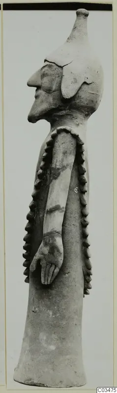 Terracotta figurine in side profile, standing, with a long neck, prominent nose and rows of applied knobs down the sides.