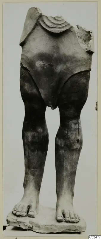 Terracotta figure with head and arms missing, standing on a flat base, legs and feet intact