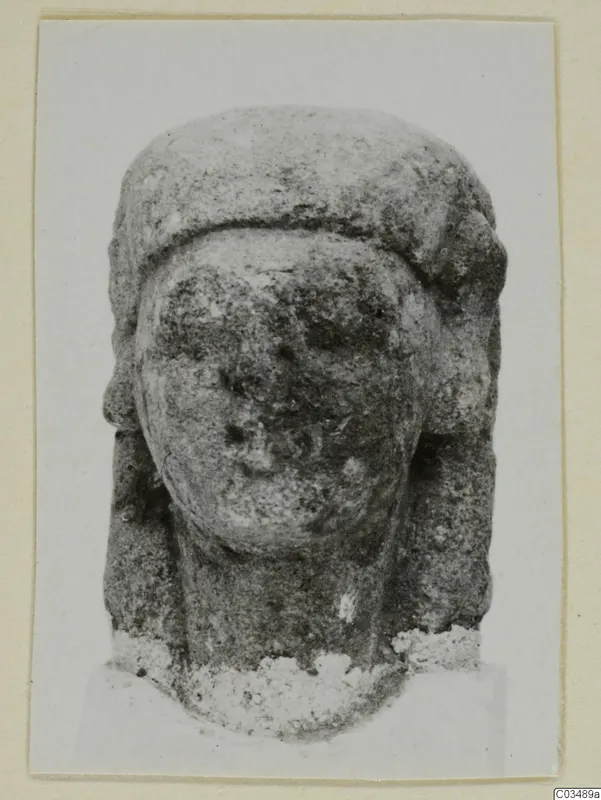 Limestone sculpture of a head with a tall headdress and worn face, seen from the front.