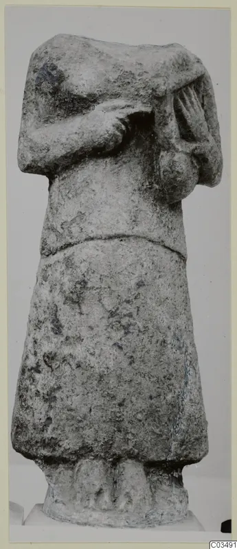 Headless limestone statue of a standing figure with arms bent across the chest.