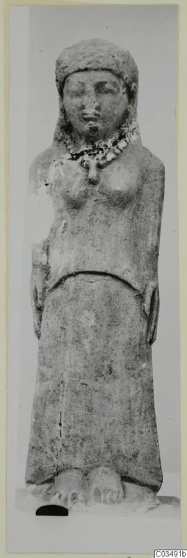 Limestone standing figure with a close-fitting head covering and necklace, arms at its sides, on a plain background