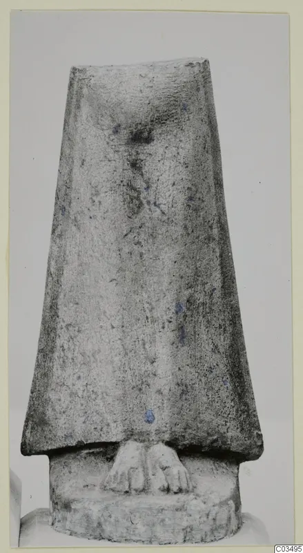Limestone sculpture of a tapering figure with two carved feet at the base, photographed against a plain grey background.