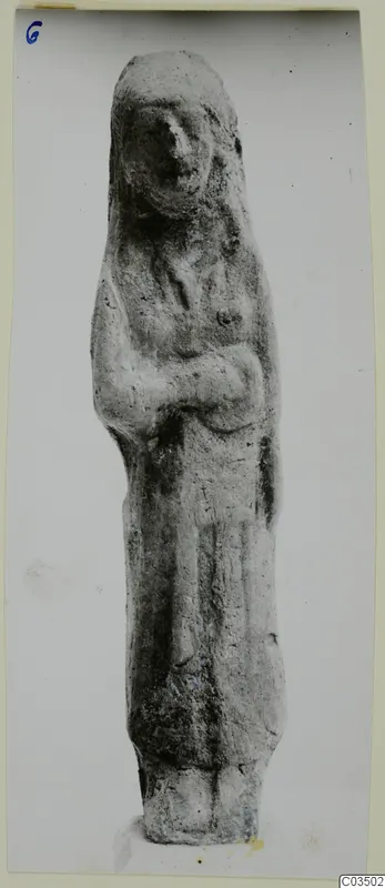Terracotta figurine of a standing figure with a covered head and arms held across the body
