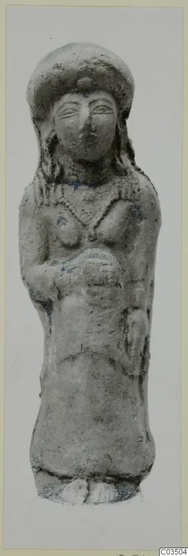 Terracotta figurine of a standing female figure with a tall headdress and curled hair, photographed against a grey background.