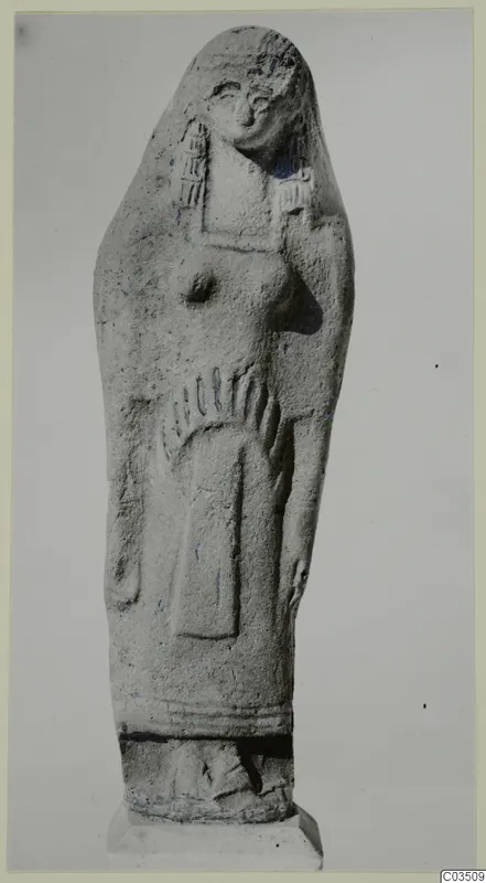 Standing female figure in grey relief, with a rounded top, raised breasts and a long garment, on a stepped base