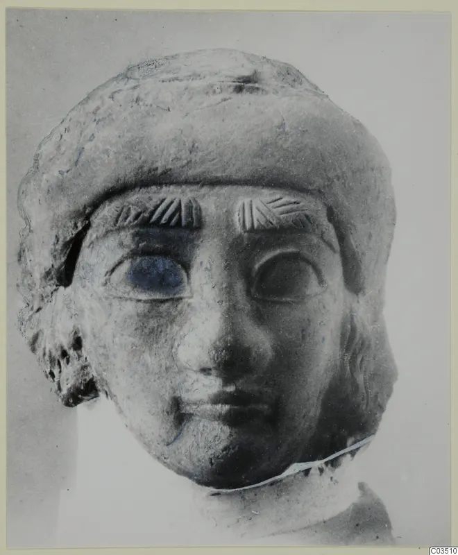 Terracotta head of a figure in a rounded cap, with hatched eyebrows and large eyes, photographed frontally.