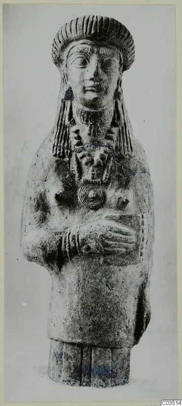 Terracotta figurine of a standing figure with a tall headdress and arms folded across the chest