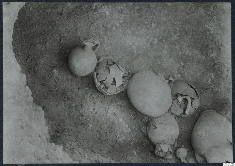 Excavated ground at Stylli with pottery vessels, a small jug and rounded bone shapes, possibly skulls