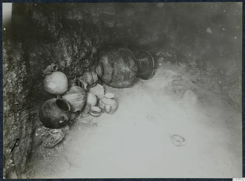 Pots and bowls lying against a rock face during excavation