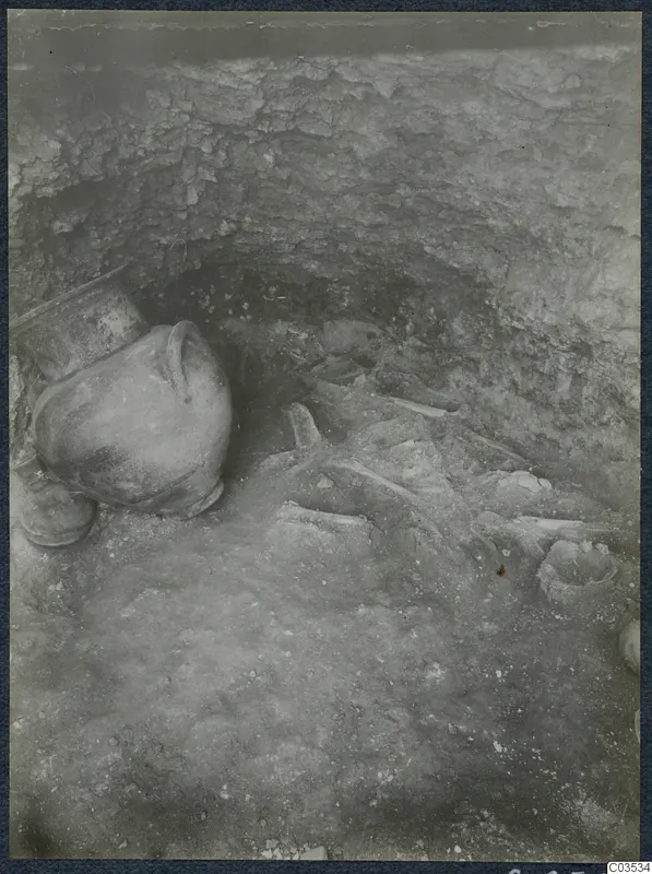 Excavation at Stylli showing a large jug on the left and scattered bones and a small bowl on the floor of the cut