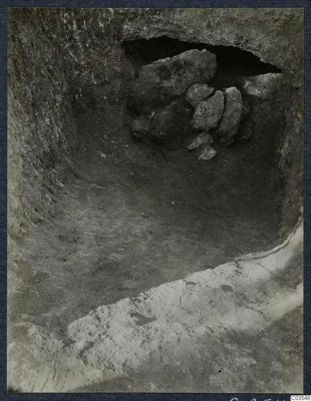 Excavation at Stylli showing a cut with a dark opening in the rock wall, partly blocked by a heap of stones