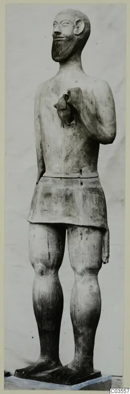 Terracotta statue of a standing bearded man in a short skirt, one hand raised to the chest.