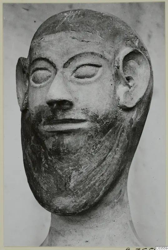 Terracotta head of a bearded man with large ears and almond-shaped eyes, shown against a pale background