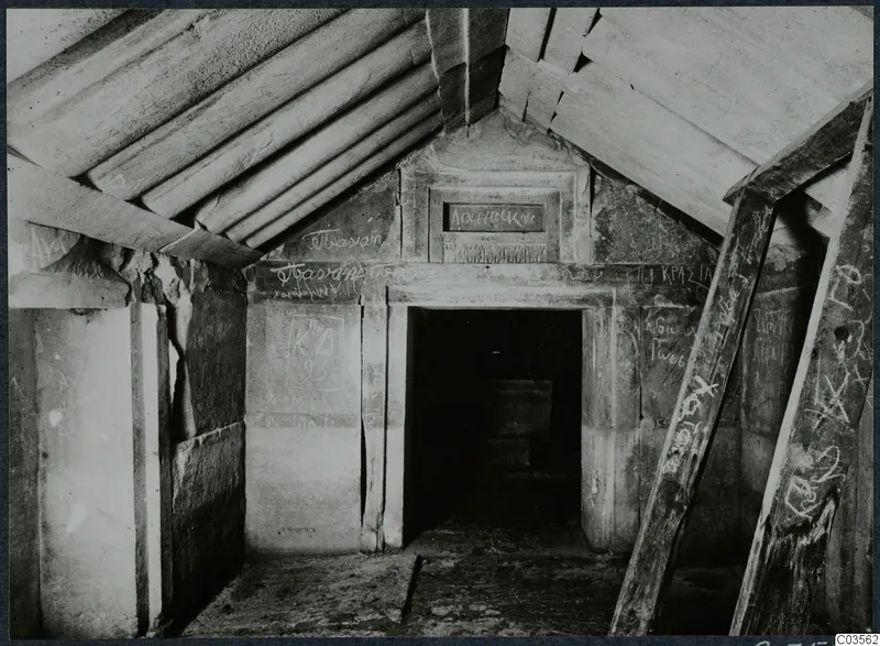 Interior of a built tomb chamber with sloping stone roof slabs, wooden props and graffiti on the walls