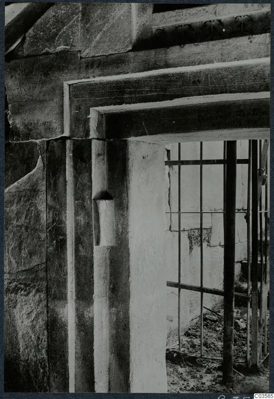 Doorway of a built tomb with a stone lintel and jamb, closed by an iron grille