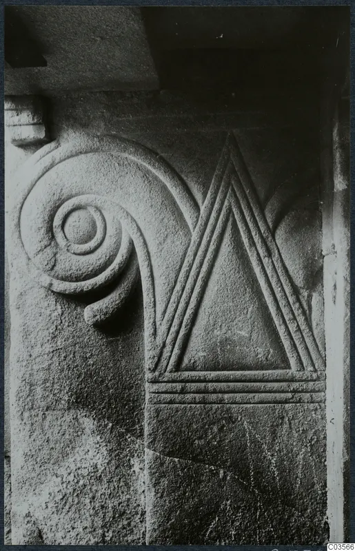 Close view of carved stone with a spiral scroll at left and a triangle outlined by raised parallel bands at right