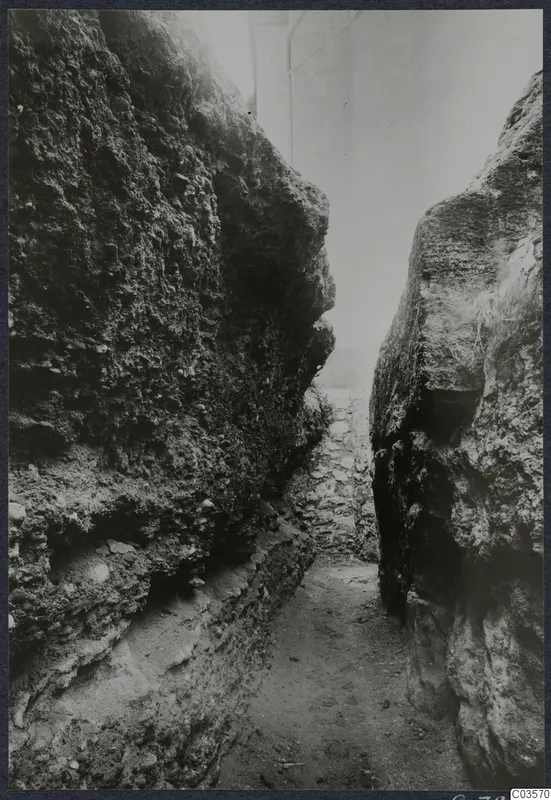 Narrow passage between tall rock faces, with a built stone wall at its far end