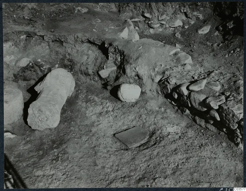 Finds in situ at Cholades, Soli: a long cylindrical stone block and rounded stones lying in excavated ground.