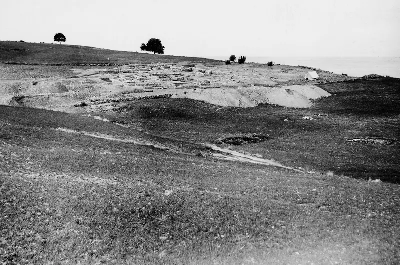 Excavated temple remains at Soli on a grassy hillside, with a small tent beside the ruins and the sea beyond.